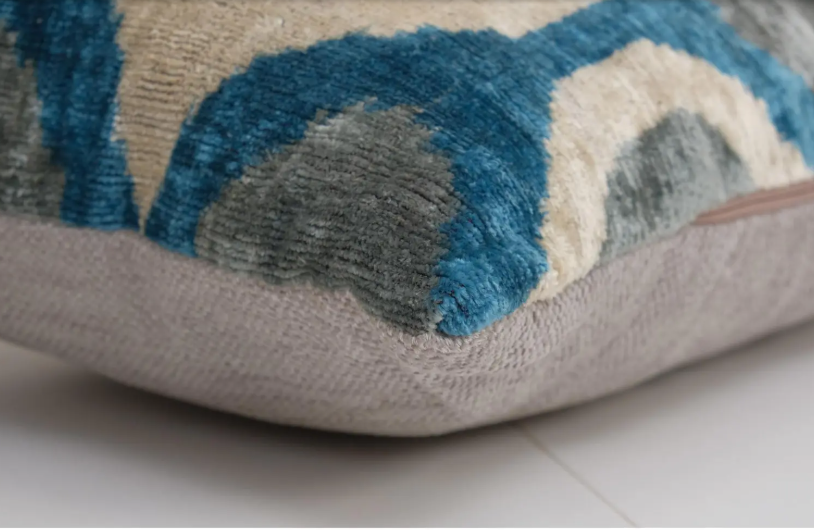 Decorative throw pillow with teal blue curved abstract pattern on beige background showing textured pile weave detail
