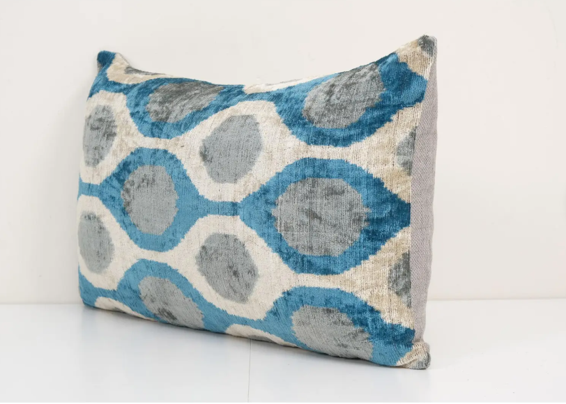 Rectangular velvet pillow with turquoise blue and gray circular ikat pattern on cream background with textured finish