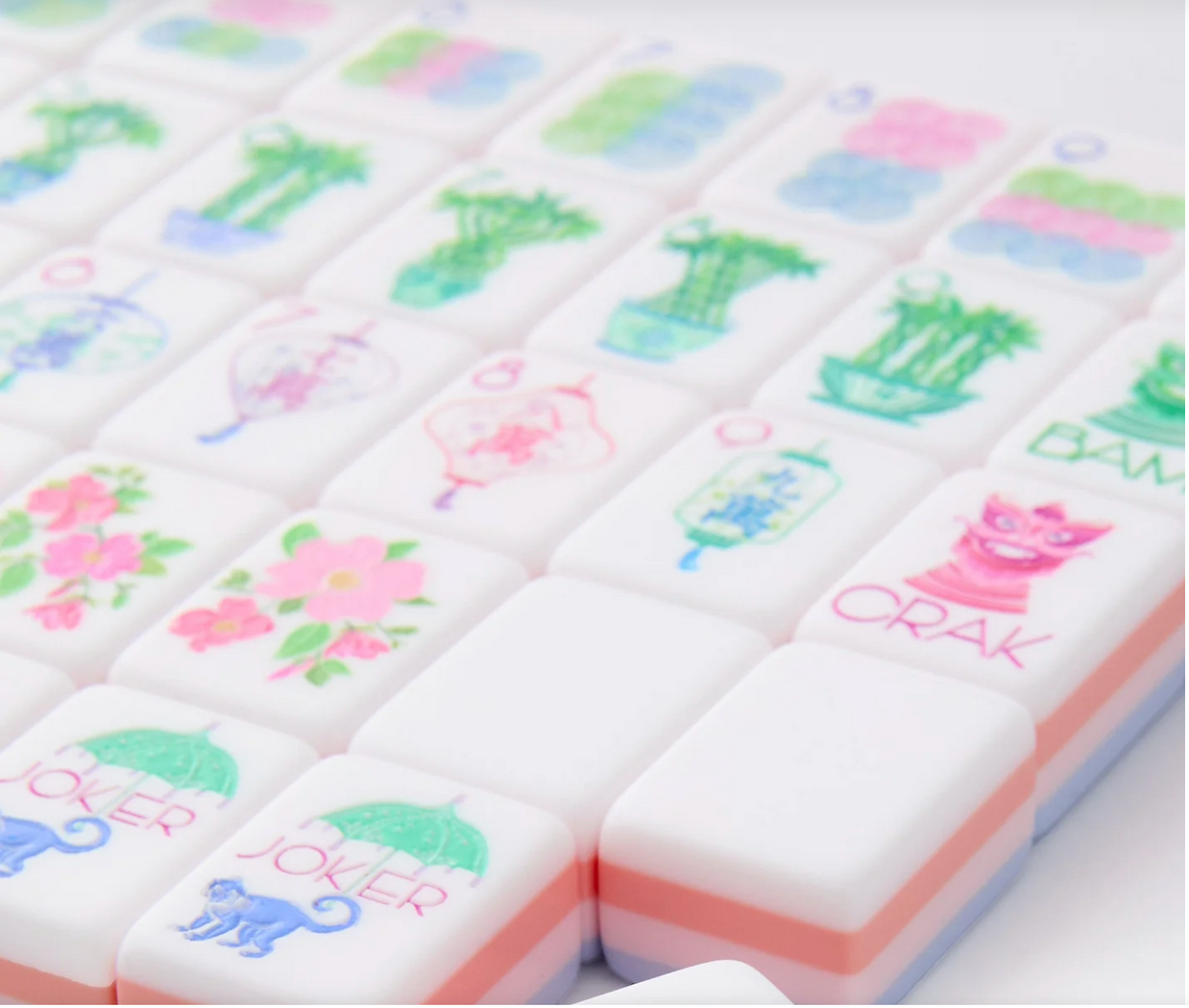White mahjong tiles with pastel green bamboo, pink flowers, and blue wave patterns on pink and blue layered backing