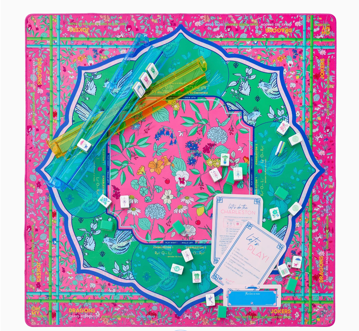 Mahjong game board with vibrant pink floral border, turquoise green playing surface, yellow tile racks, and scattered white tiles