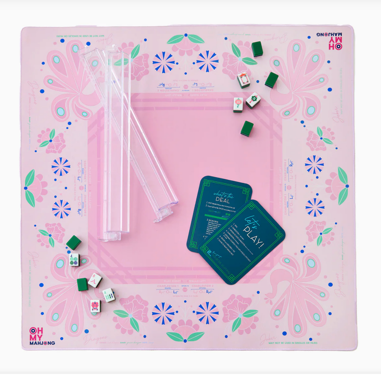Mahjong game mat in pink with peacock and floral motifs, clear plastic tile racks, and teal instruction cards centered