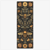 Black yoga mat with symmetrical folk art pattern featuring golden bees, sage green leaves, and orange floral motifs.