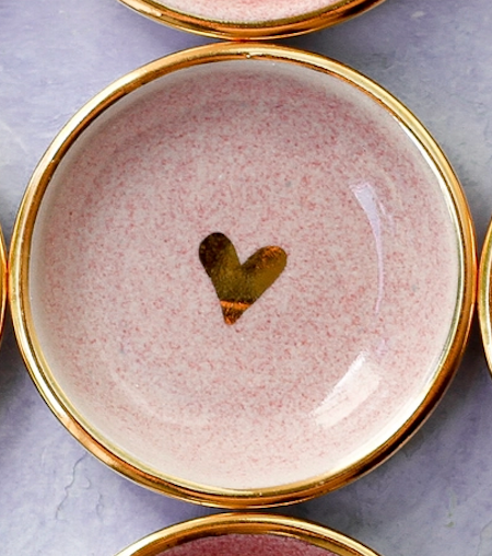 Pink speckled ceramic plate with gold rim and small gold heart accent in center on gray marble surface