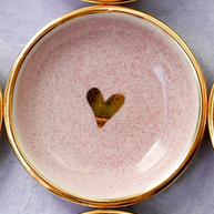 Pink speckled ceramic plate with gold rim and small gold heart accent in center on gray marble surface