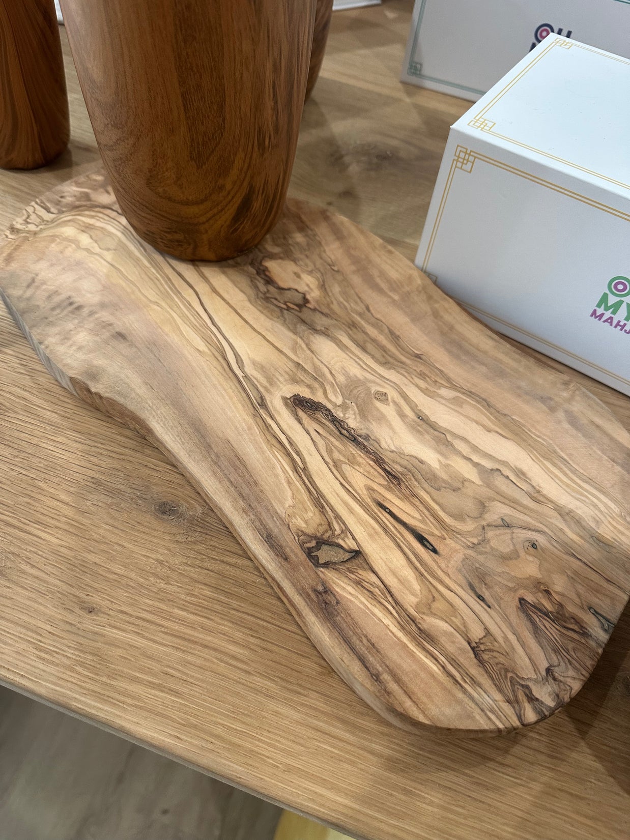 Oval olive wood serving board with rich marbled grain pattern and natural knots, displayed on light wood surface