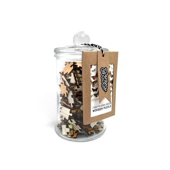 Clear glass jar with round lid filled with wooden jigsaw puzzle pieces, kraft paper hang tag with black and white twine