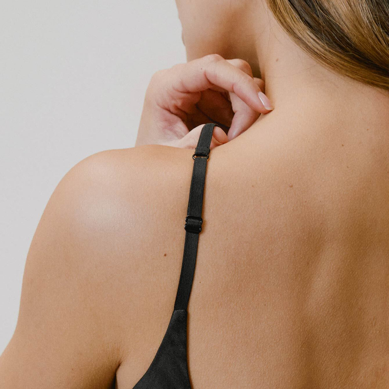 Black adjustable bra strap with gold metal slider shown on bare shoulder against neutral background