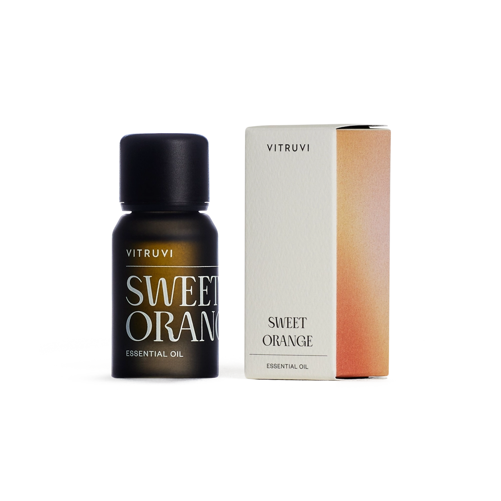 Dark amber glass bottle of Vitruvi Sweet Orange Essential Oil with black cap beside orange gradient packaging box