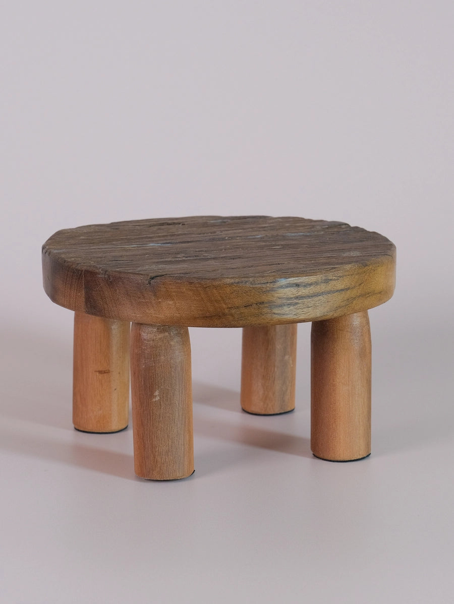 Small round wooden stool with thick grain-textured top and four cylindrical legs in natural light brown finish