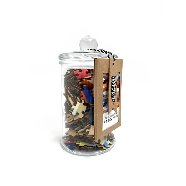 Clear glass jar with round knob lid filled with colorful wooden jigsaw puzzle pieces and kraft paper tag attached