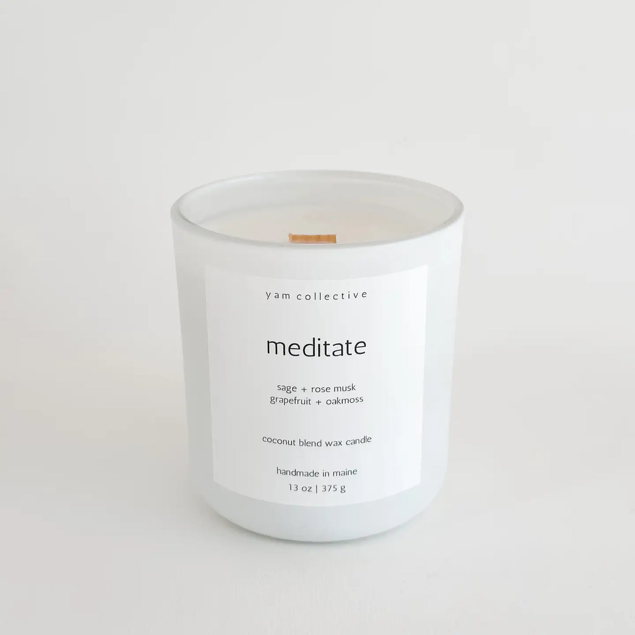 White frosted glass candle with wooden wick and minimalist label reading "meditate" by yam collective, 13 oz coconut wax blend