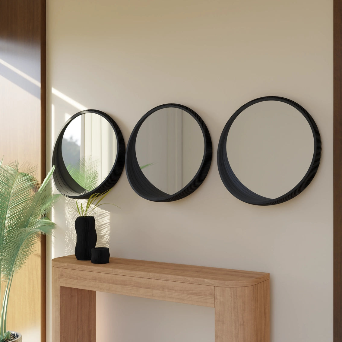 Set of three black round mirrors with textured ridged frames mounted on cream wall above wooden console table
