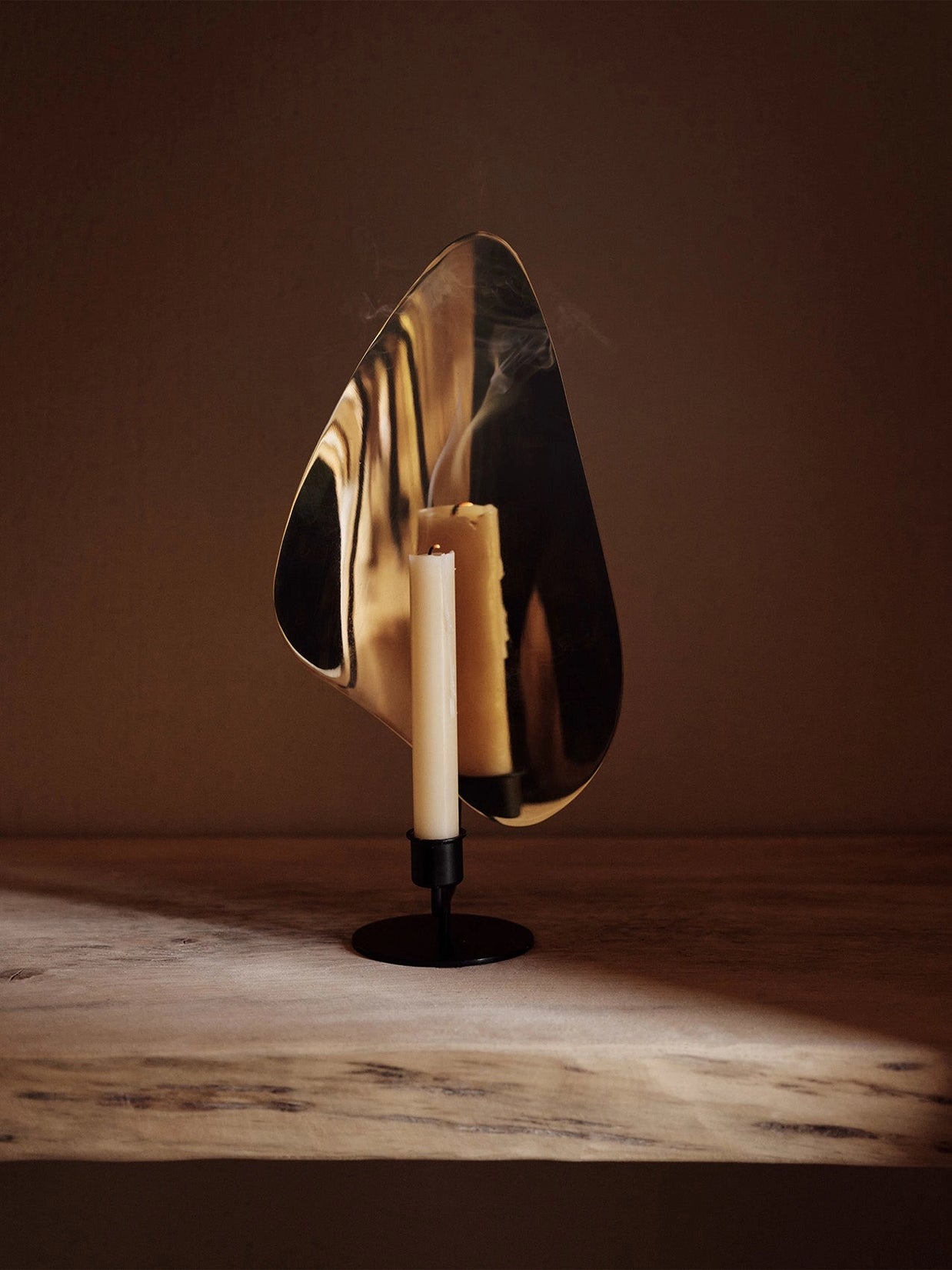 Three cream pillar candles with black bases displayed against curved brass mirror on matte black pedestal stand