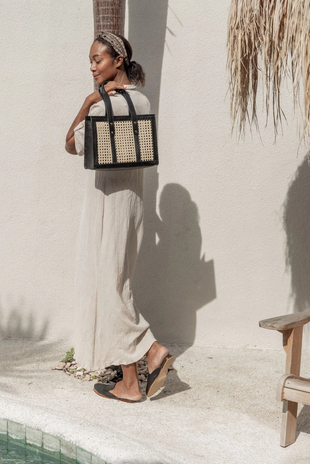 Structured tote bag with natural woven rattan panels framed by black leather trim and dual top handles with brass hardware