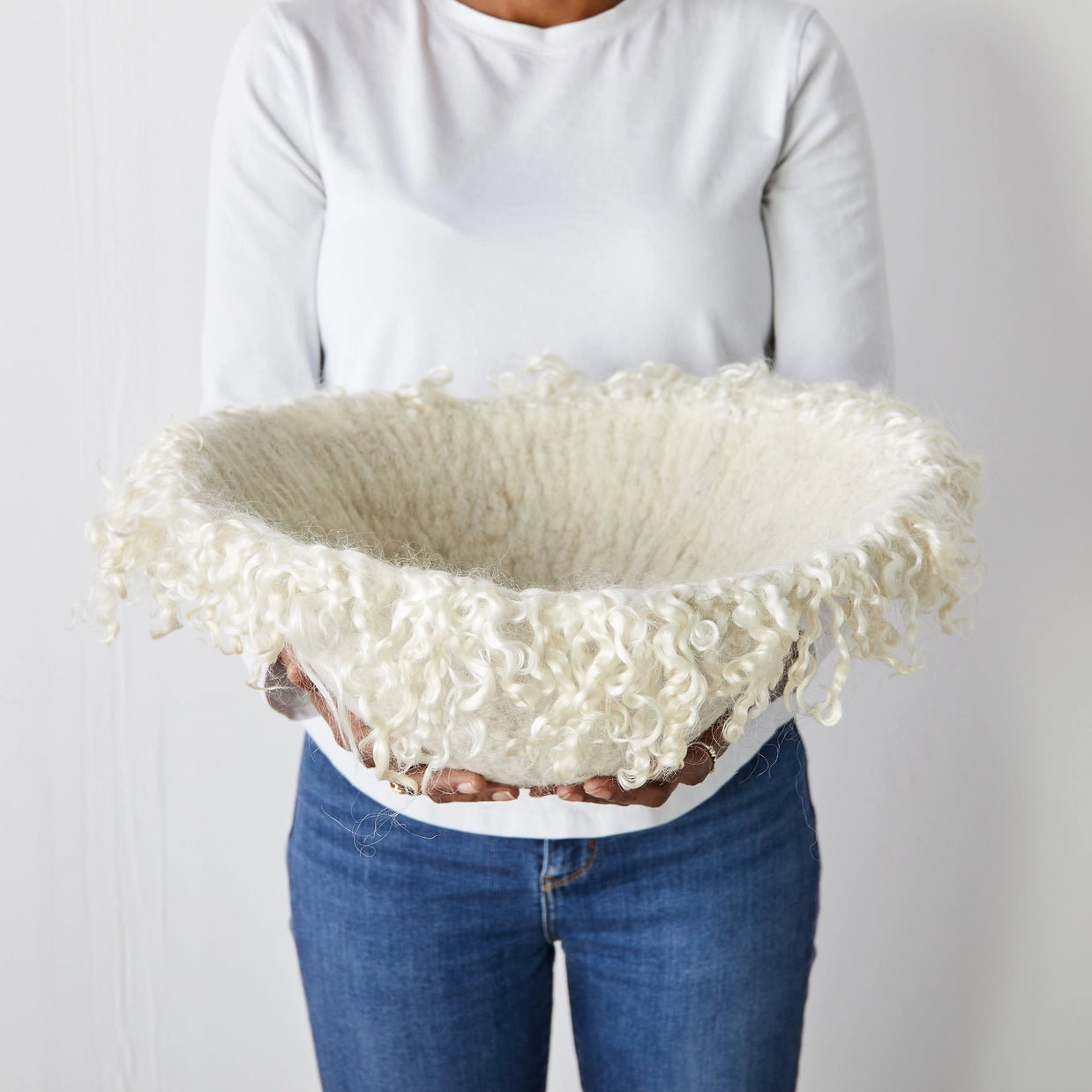 Cream colored curly wool fleece basket with natural textured edges held by person in white sweater and blue jeans