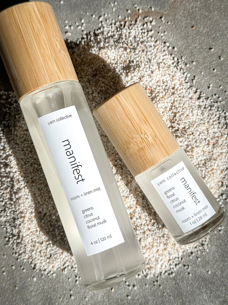 Two glass room and linen mist bottles with natural bamboo caps labeled "manifest" in 4oz and 1oz sizes on textured surface