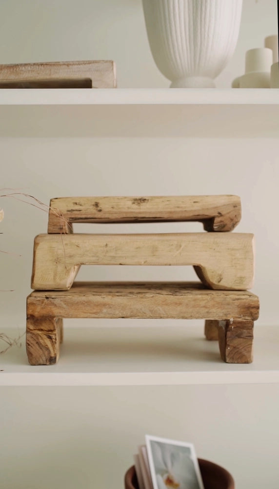 Set of three rustic wooden risers with weathered finish and rectangular cutout handles, stacked on white shelf