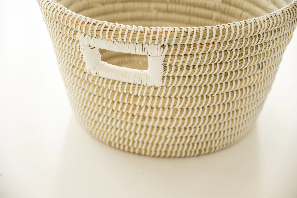 Handwoven storage basket in natural tan and cream with coiled stripe pattern and rectangular cutout handle on white background
