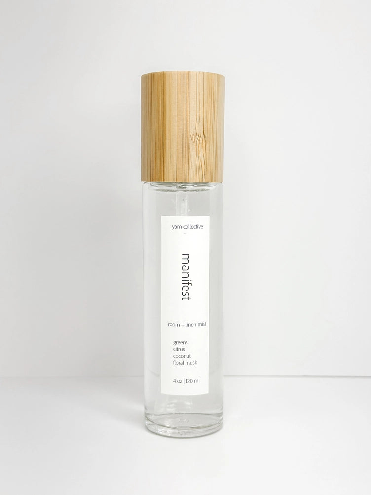 Clear glass spray bottle with natural bamboo wood cap and white label reading manifest room and linen mist