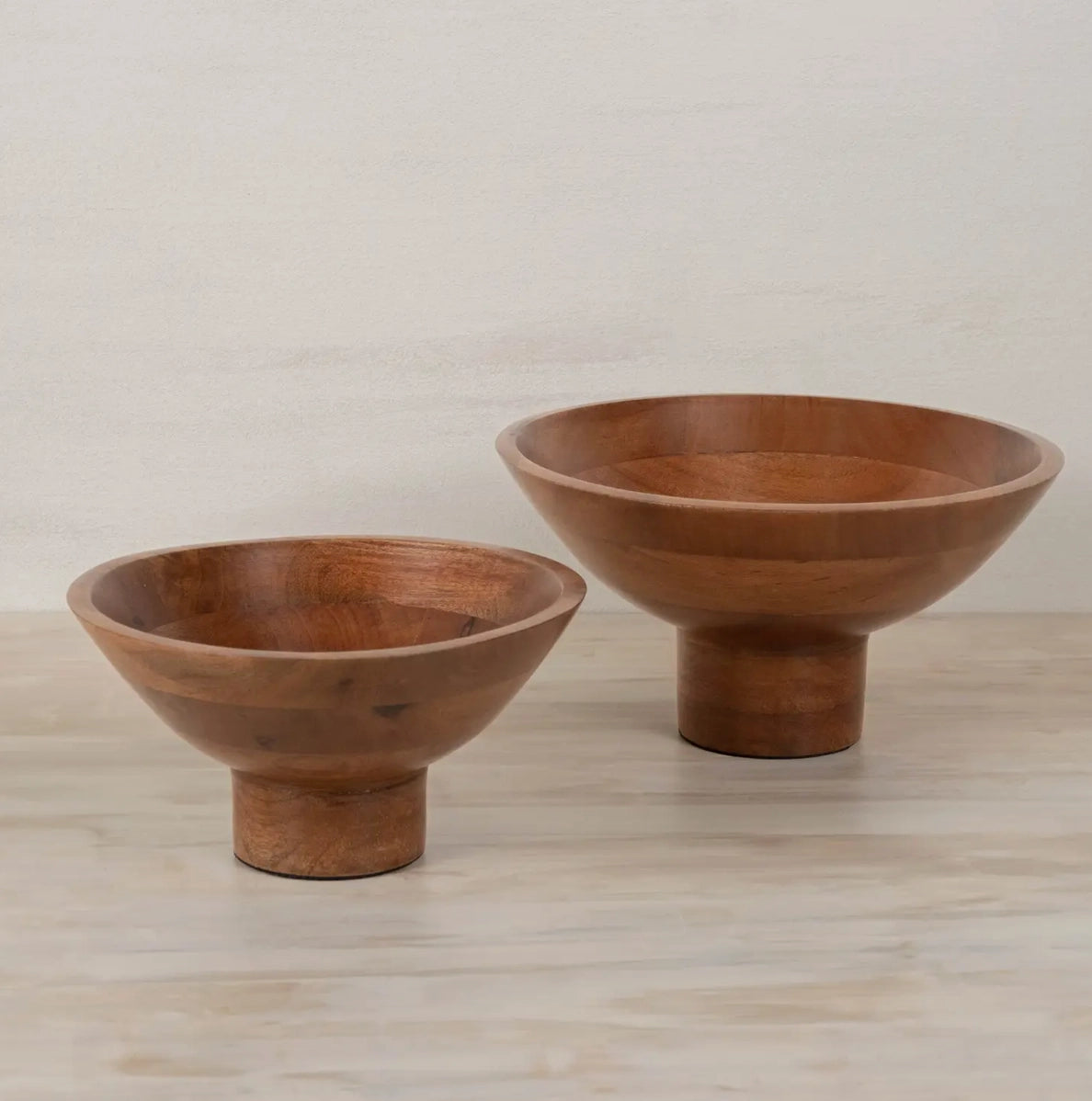 Two turned wood pedestal bowls in warm brown tones with visible grain, cylindrical bases, shallow rounded profiles