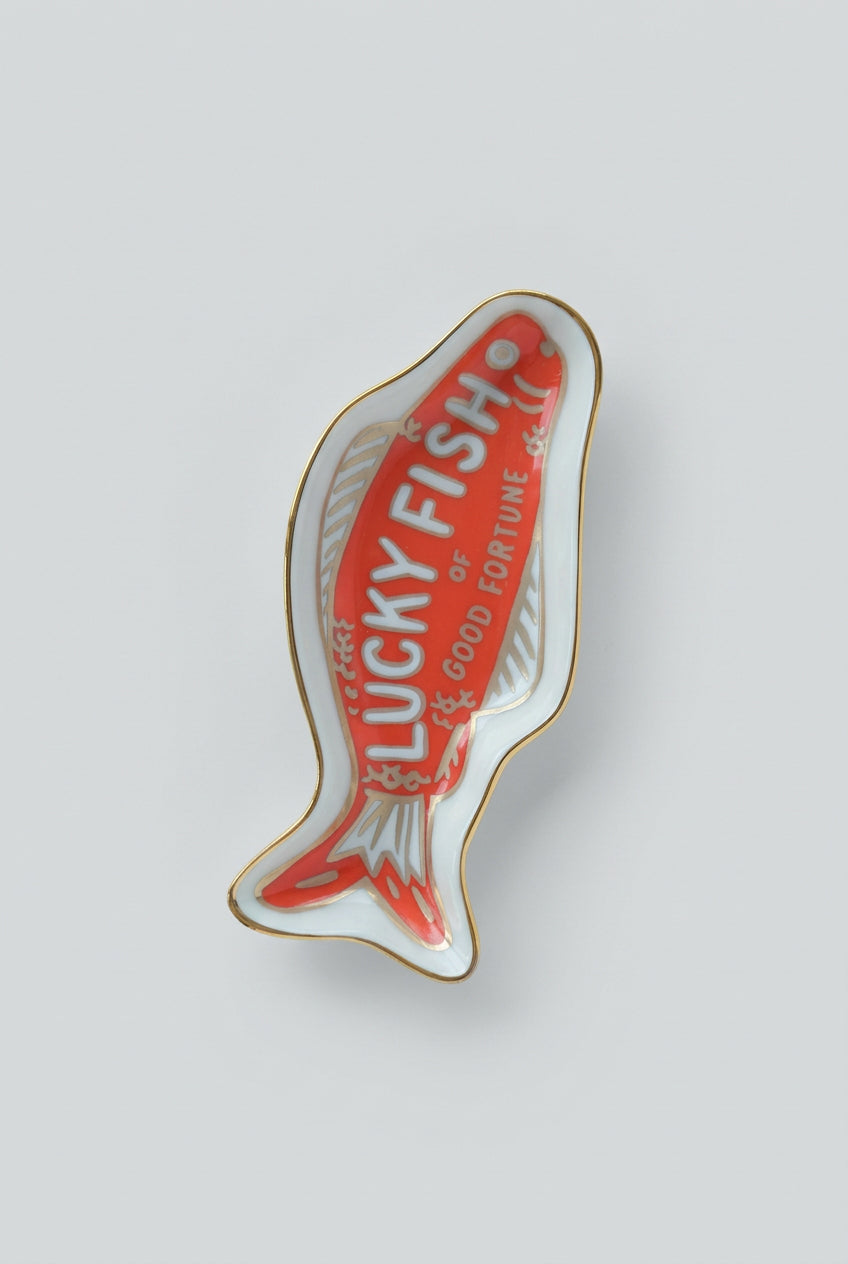 A fish-shaped ceramic dish or tray with a red center, white outer area, gold trim, and the words 'LUCKY FISH or GOOD FORTUNE' printed on it.