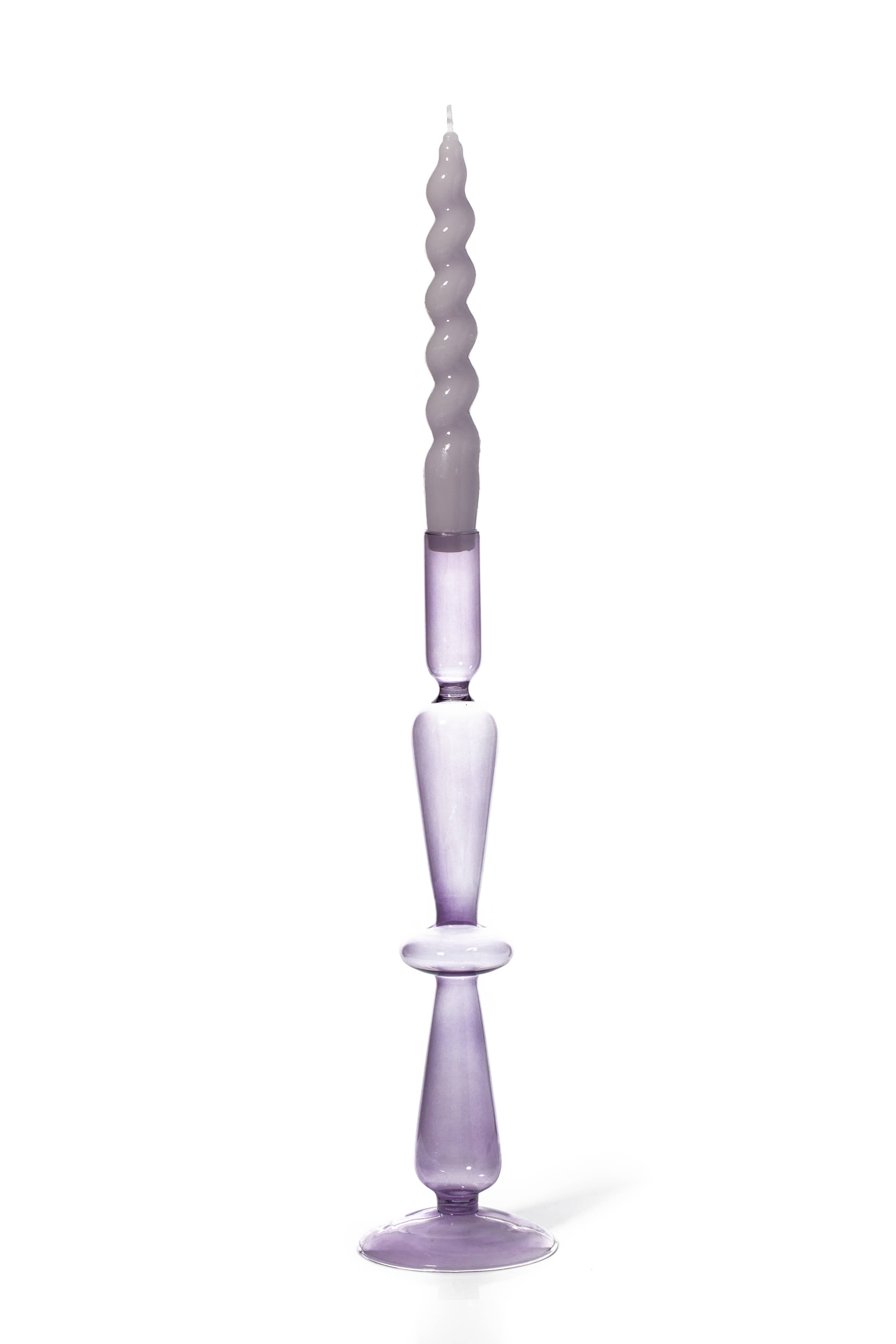 A tall, slender lavender purple glass candlestick holder with a twisted spiral taper candle inserted, set against a plain white background.