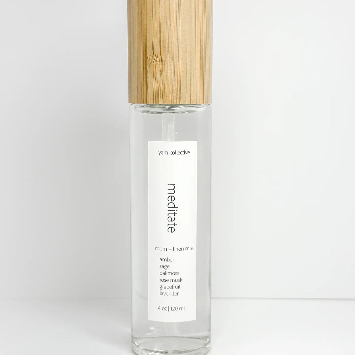 Clear glass room spray bottle with natural bamboo cap and white meditate label listing amber sage oakmoss scent notes