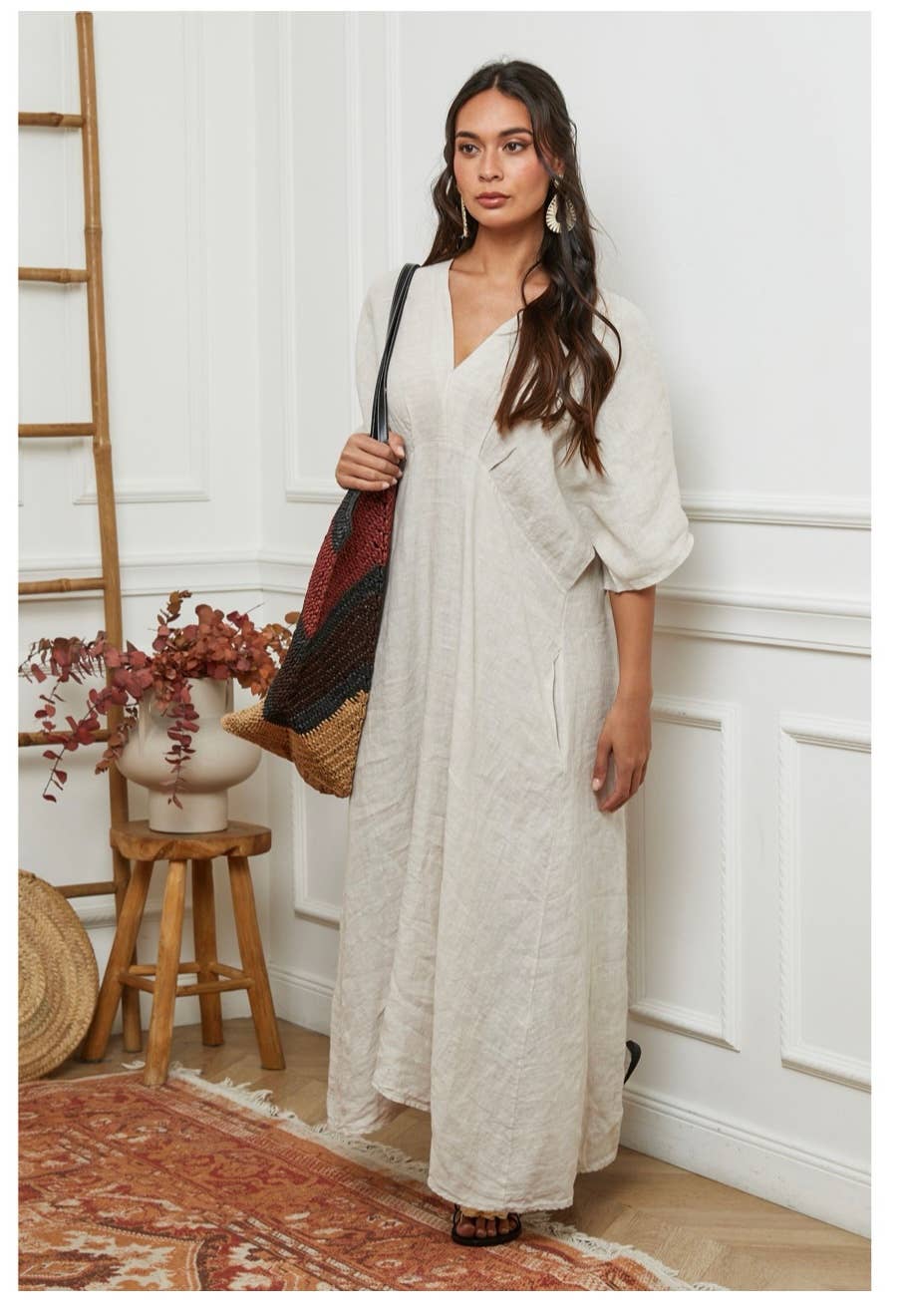 Cream linen wide-leg jumpsuit with V-neck, three-quarter sleeves, and relaxed fit styled with woven straw tote bag