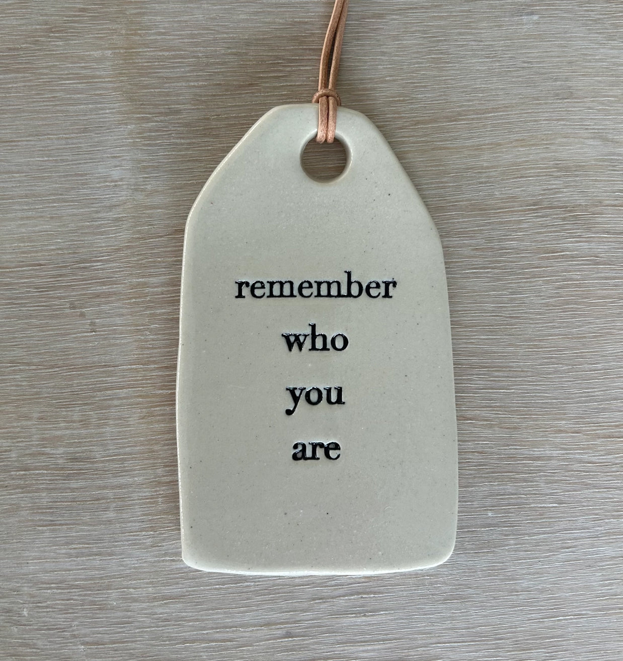 White ceramic gift tag with rounded edges and leather cord stamped with remember who you are in black text