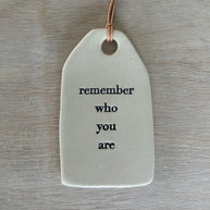 White ceramic gift tag with rounded edges and leather cord stamped with remember who you are in black text