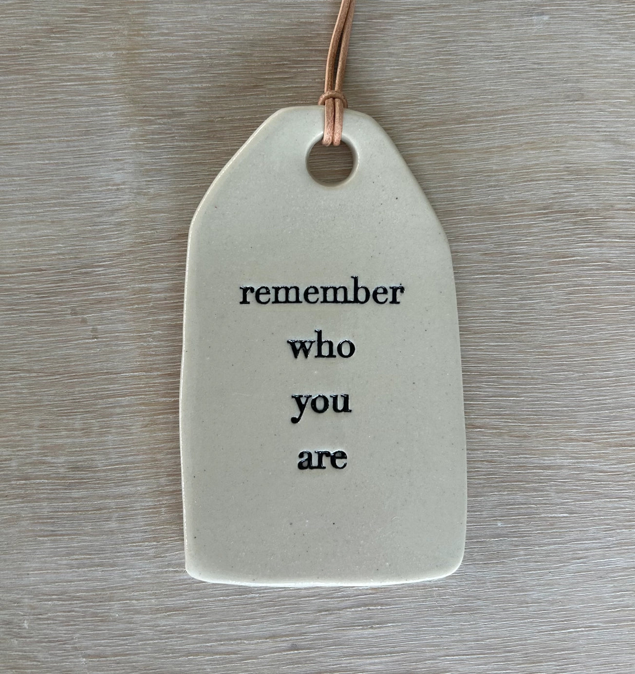 White ceramic gift tag with rounded edges and leather cord stamped with remember who you are in black text