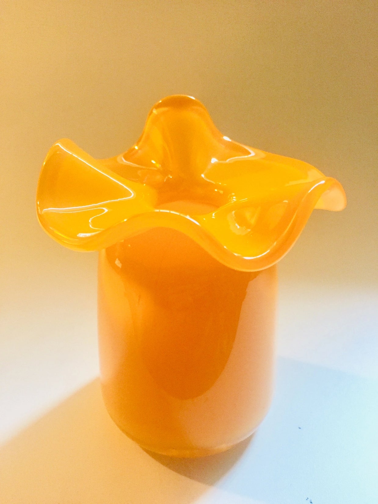Amber orange art glass vase with ruffled wavy rim and cylindrical base in glossy finish on neutral background