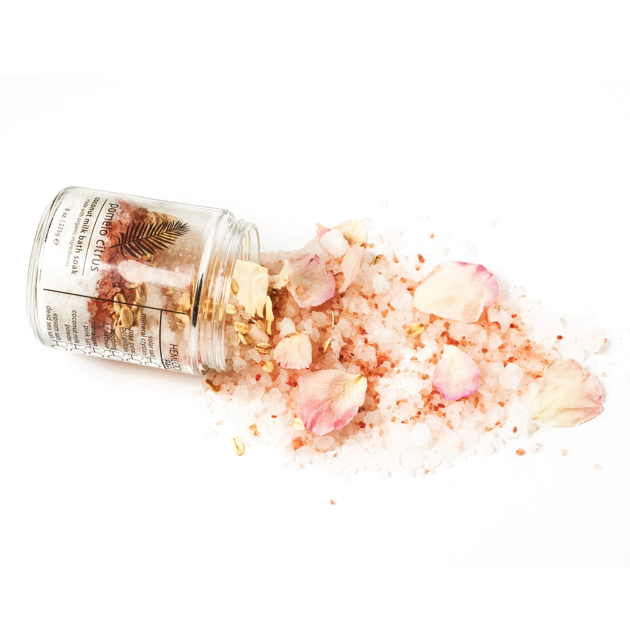 Glass jar tipped over spilling pink Himalayan salt crystals mixed with rose petals, dried flowers, and gold leaf flakes