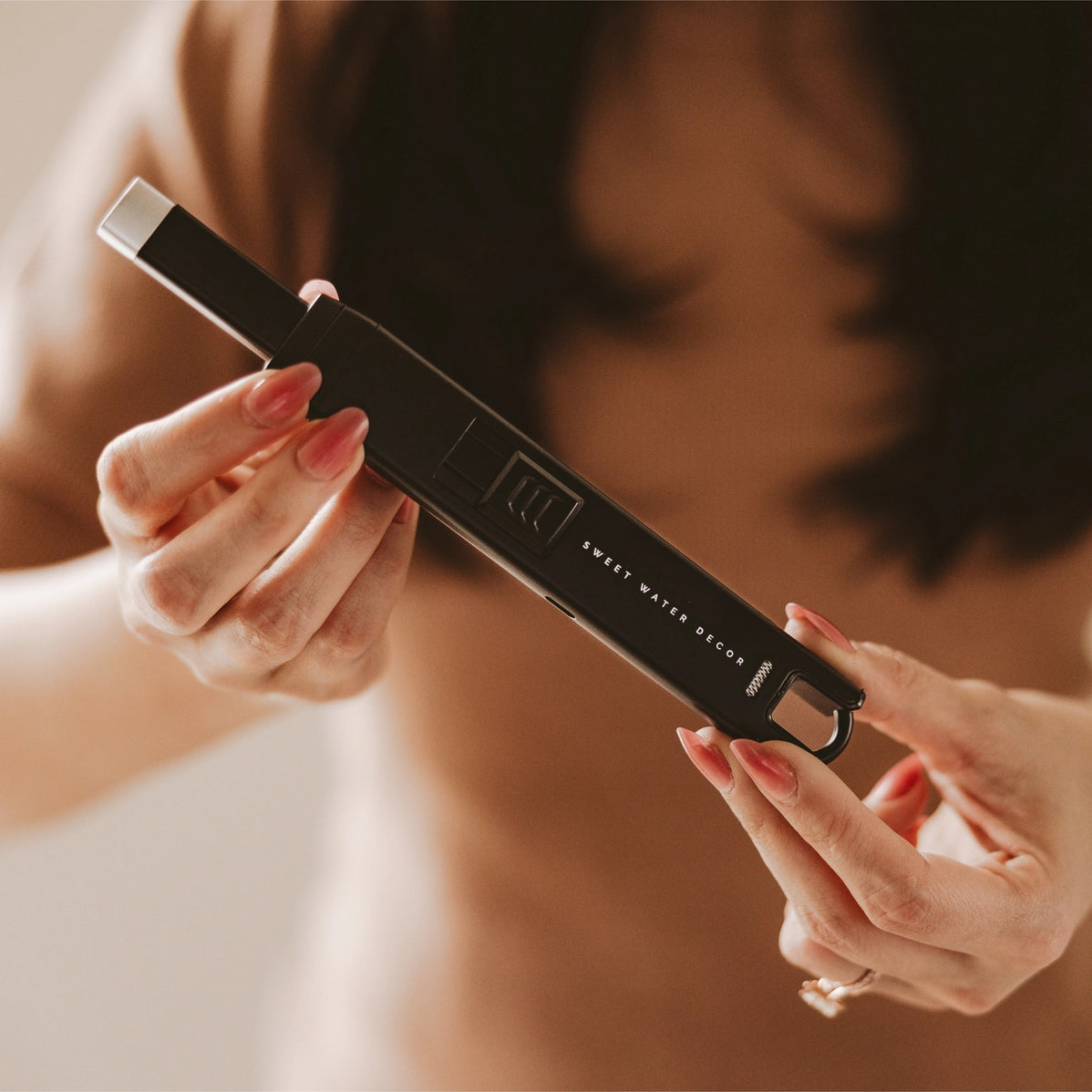 Sleek black rectangular perfume bottle with silver cap and Sweet Water Decor branding held in hands with pink manicure