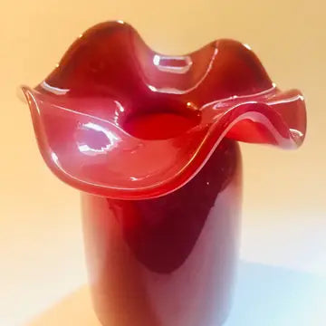 Deep crimson red glass vase with ruffled organic wavy rim and glossy smooth finish on neutral background