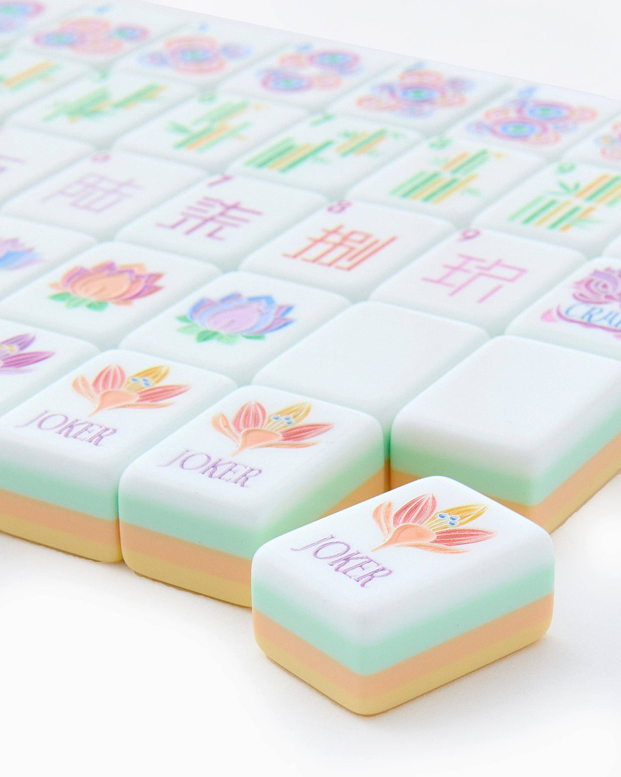 Pastel mahjong tiles in mint green and cream with colorful floral designs, bamboo patterns, and Chinese characters on white surface
