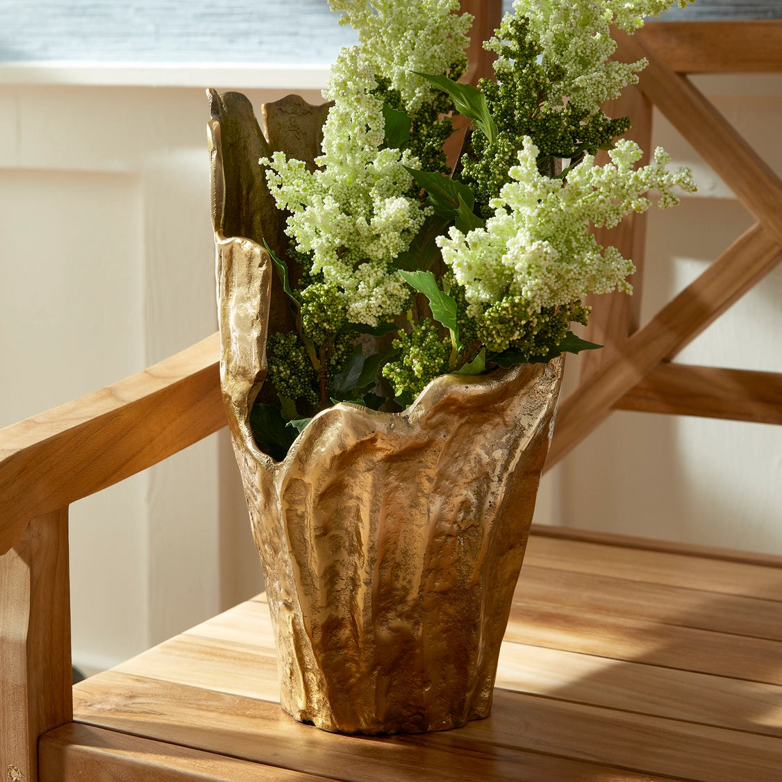 Rustic teak wood root vase with organic irregular shape holding cream and green hydrangea stems on wooden stairs