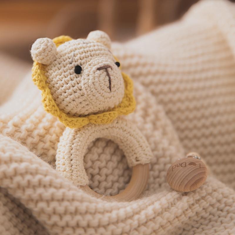 Handmade crochet lion baby rattle in cream yarn with golden yellow mane and wooden teething ring on knit blanket