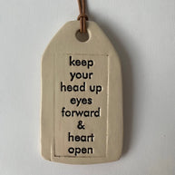 Cream ceramic tag with brown leather cord displaying inspirational quote in black text on textured surface
