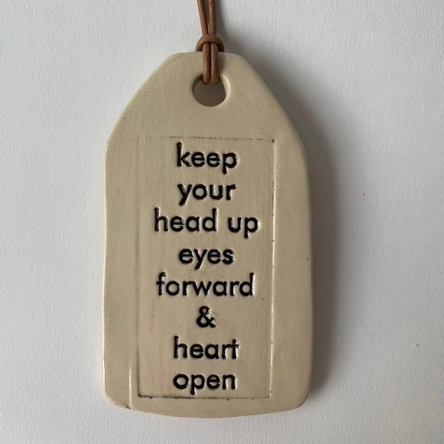 Cream ceramic tag with brown leather cord displaying inspirational quote in black text on textured surface