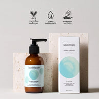 MadHippie cream cleanser amber glass pump bottle with aqua watercolor label beside white product box on speckled stone blocks