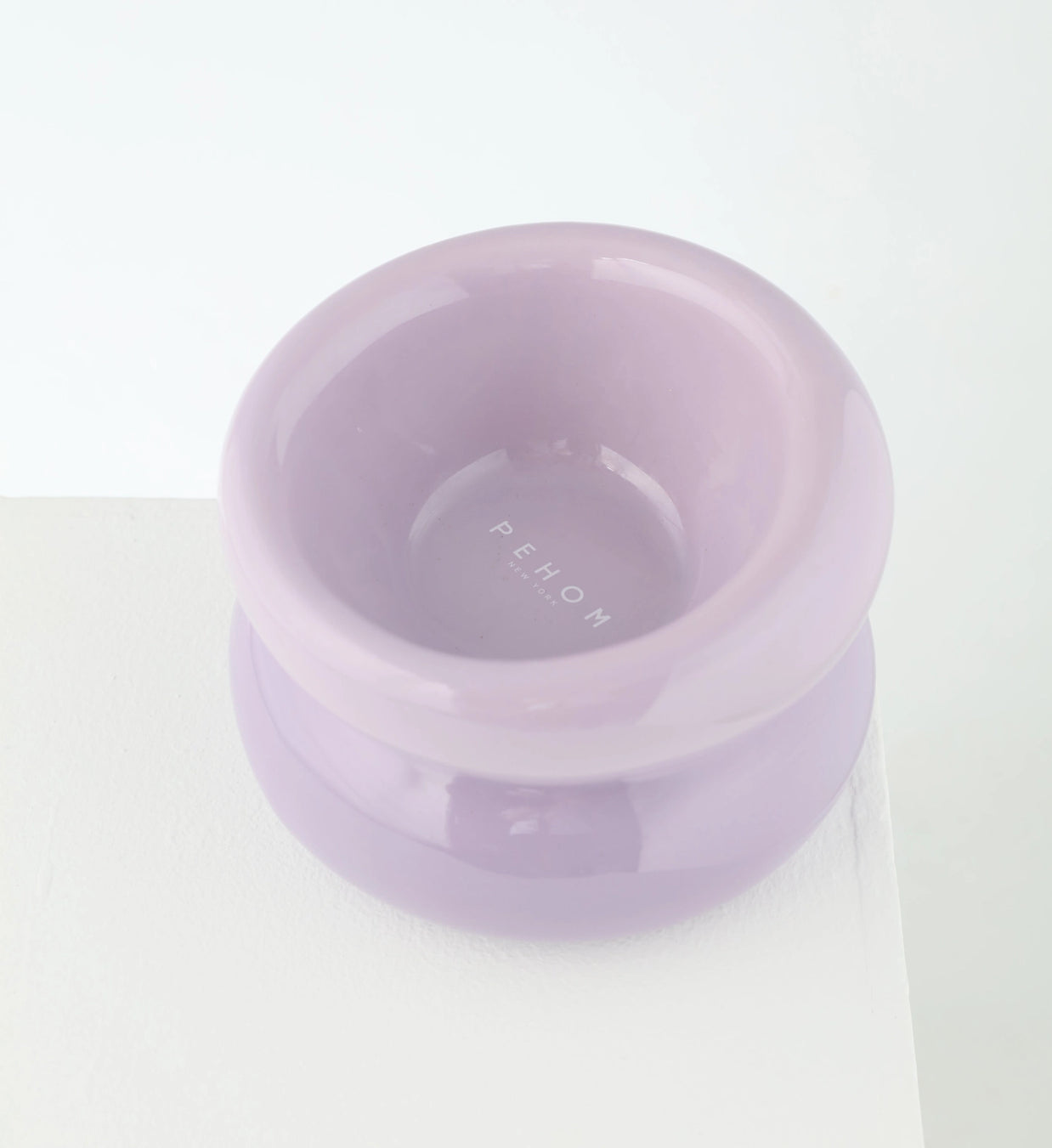 Elevated ceramic pet bowl in soft lavender with embossed brand name on interior and wide stable base on white surface