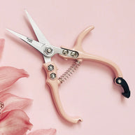 Pink-handled scissors with silver blades on a pink background with floral elements