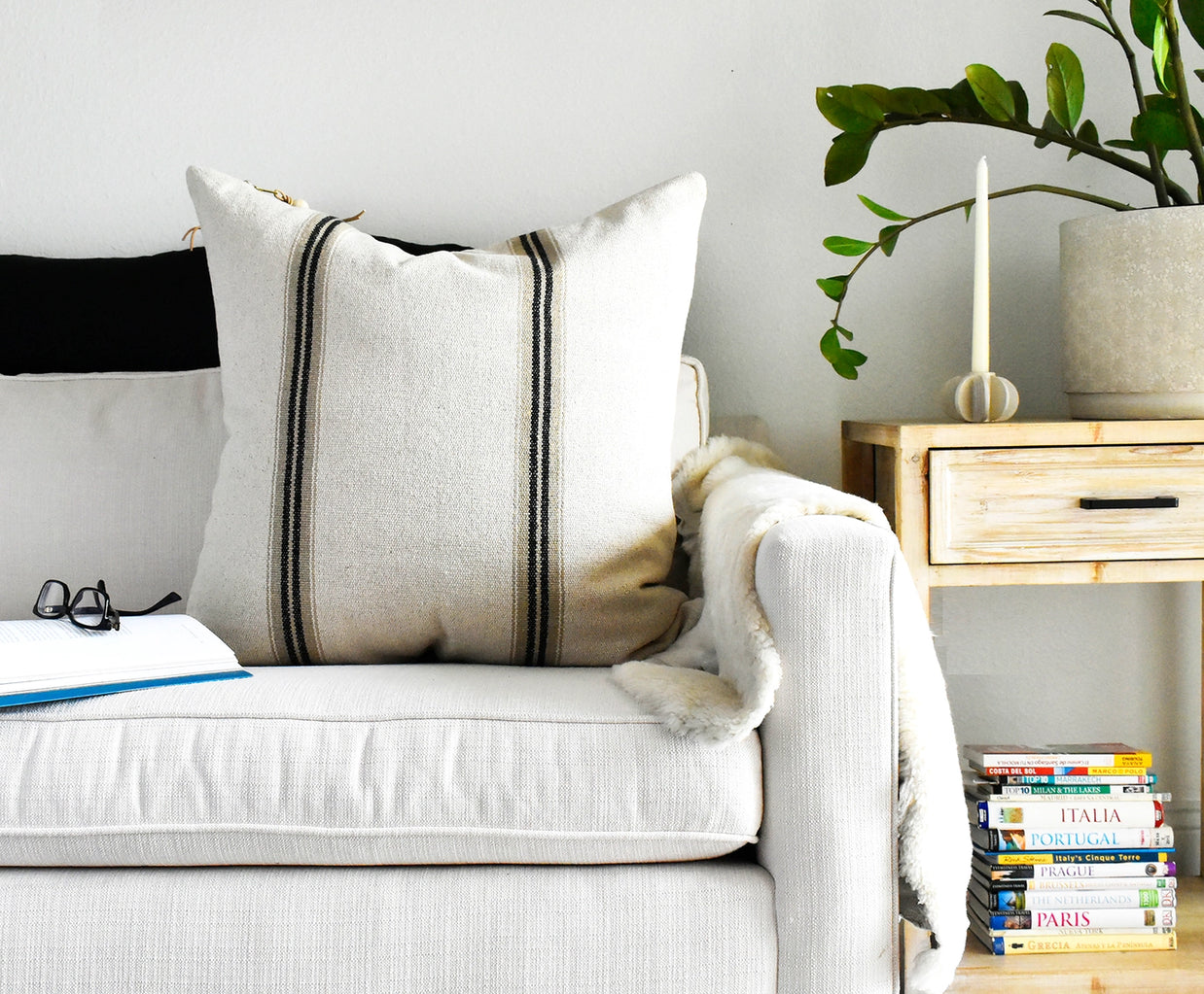 Cream linen throw pillow with black vertical grain sack stripes, featuring textured fabric and leather corner tabs