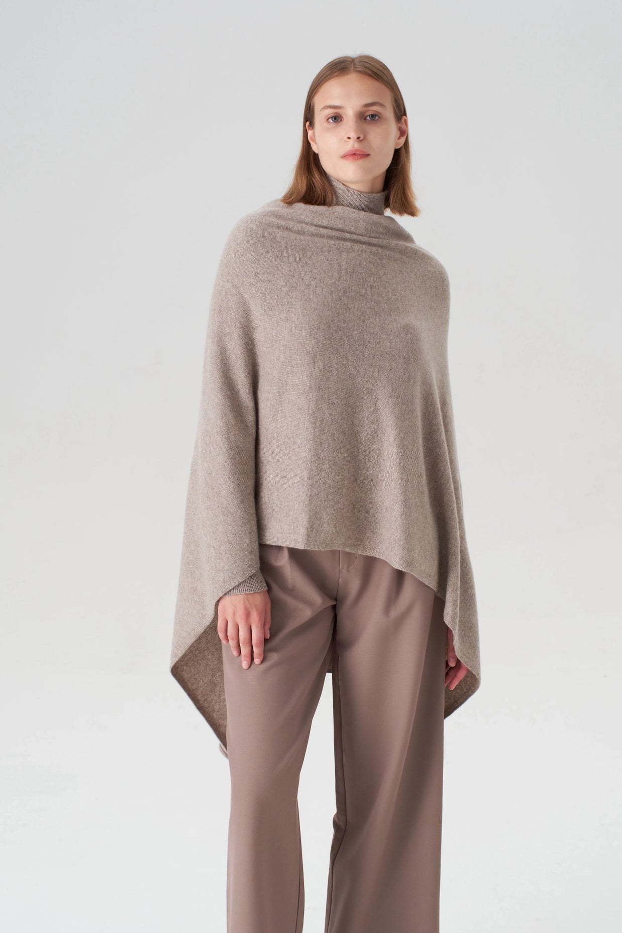 Taupe cashmere poncho with asymmetric draped hem and ribbed turtleneck collar paired with matching wide-leg trousers