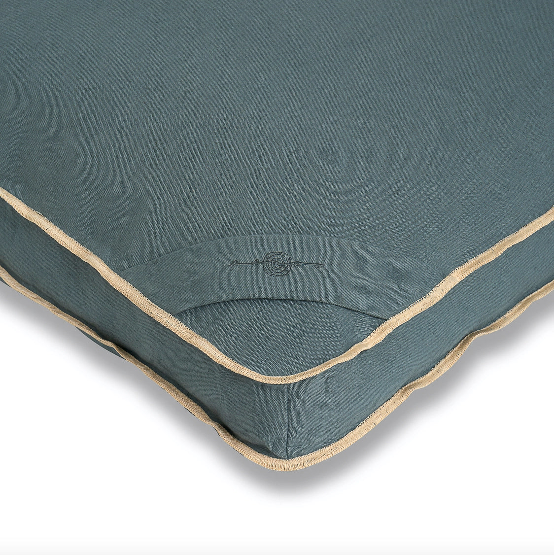 Teal blue-green cushion with taupe piped edges and embroidered logo detail on quilted fabric surface