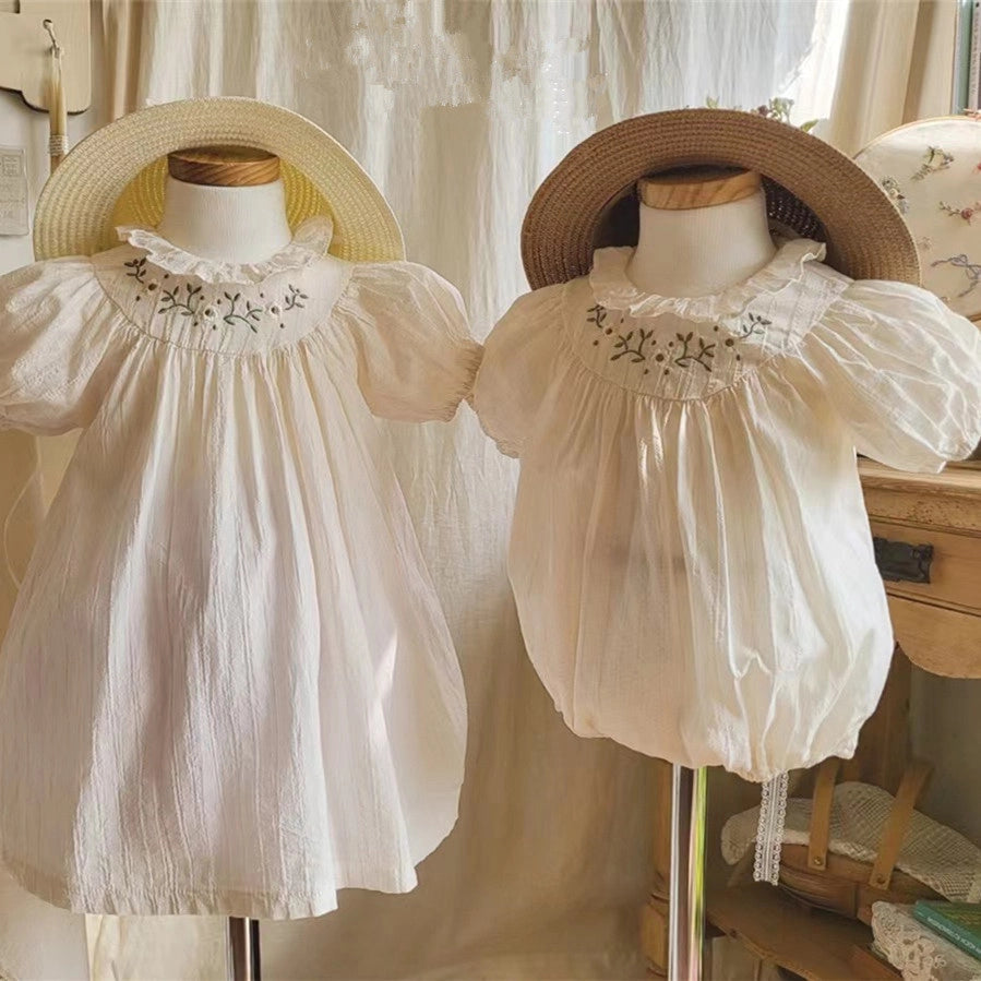 White cotton smocked dress and bloomer set with floral embroidery on ruffled neckline and puff sleeves displayed on mannequins