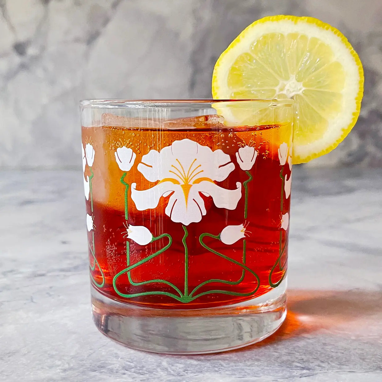 Vintage rocks glass with white iris flower pattern filled with amber-red cocktail garnished with fresh lemon wheel