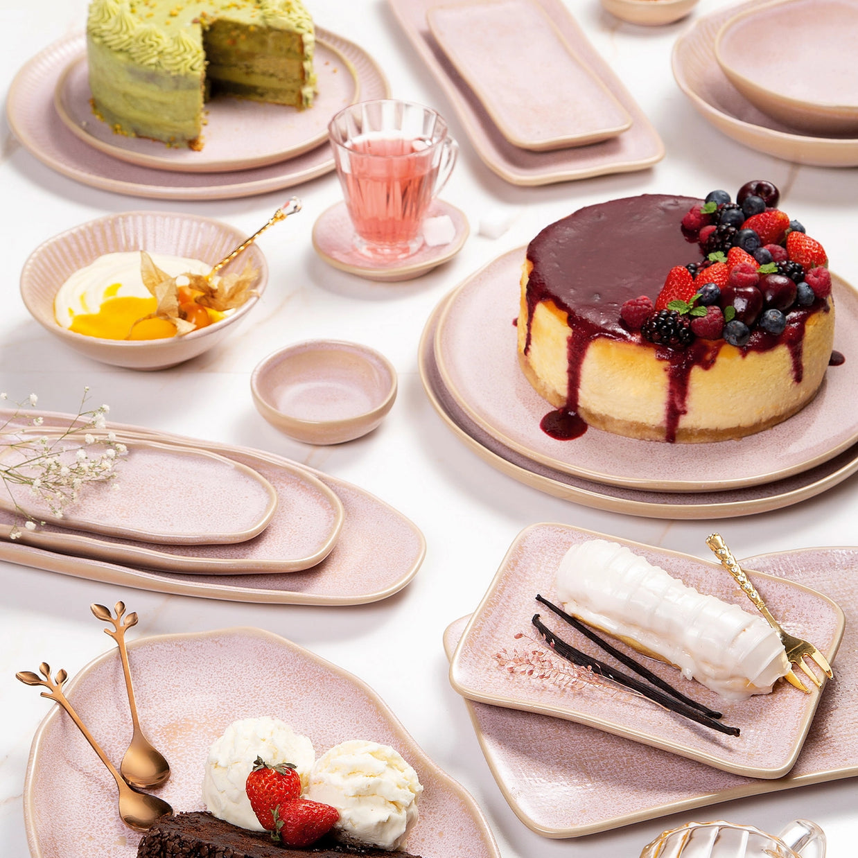 Blush pink ceramic dinnerware set with gold rim displaying cheesecake, layer cakes, and desserts in flatlay arrangement