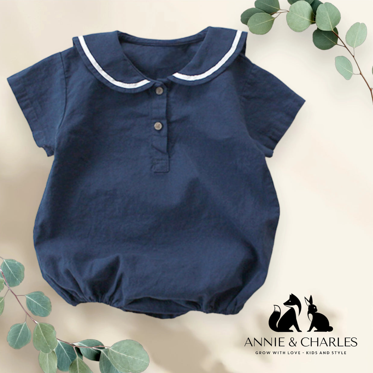 Navy blue cotton baby romper with white-trimmed Peter Pan collar, short sleeves, two-button placket, and gathered leg openings